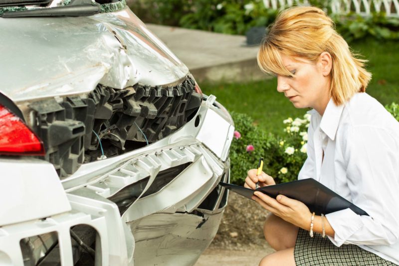 Female Adjuster Looking At Crashed Car