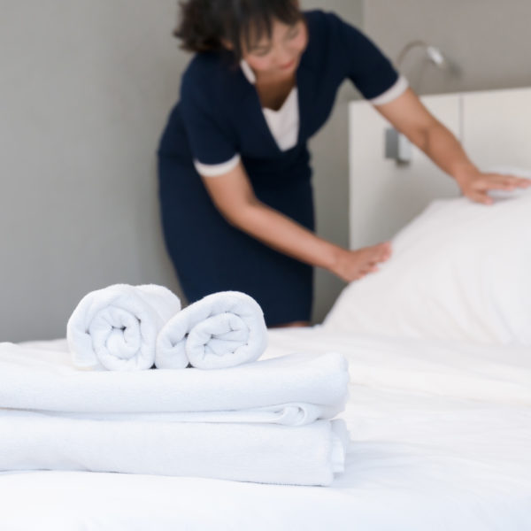 Hotel room service. Young maid making bed in a roo